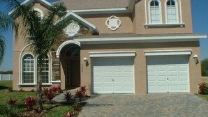 A two-story house with a stone facade, two garage doors, and a landscaped front yard with palm trees and red plants. - Ip60215 - Sand Hill - 5 Bed 3 Baths Villa (Davenport)