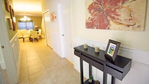 A hallway with a dining area, a black console table with a picture frame, and a large abstract painting on the wall. - Fv52288 - Paradise Palms - 5 Bed 4 Baths Townhome (Kissimmee)