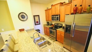 A kitchen with granite countertops, stainless steel appliances, wooden cabinets, and a wall clock. - Fv52288 - Paradise Palms - 5 Bed 4 Baths Townhome (Kissimmee)