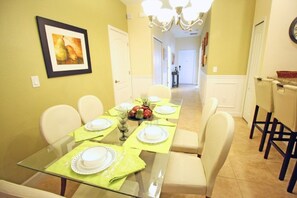 Een eetruimte met een glazen tafel voor zes personen, stoelen en een kroonluchter.