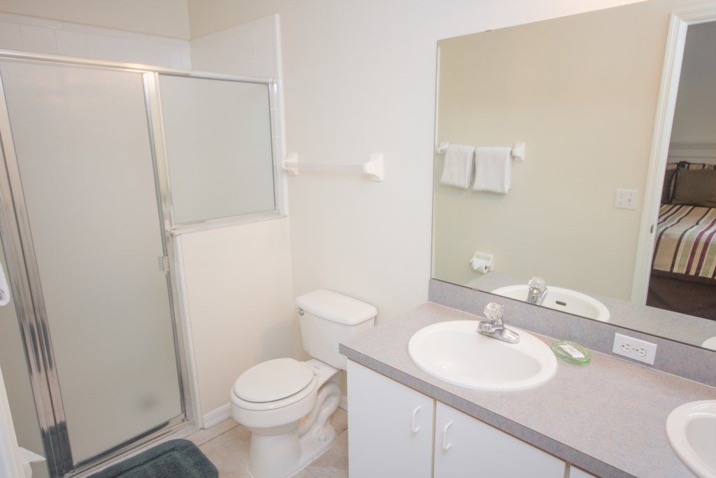 A bathroom with a shower, toilet, sink, and a large mirror.