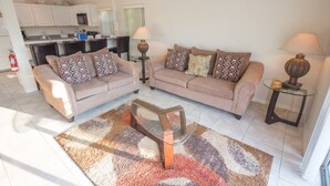 A living room with two sofas, a coffee table, and two lamps. There is a kitchen in the background. - Ip60224 - Rolling Hills Estates - 4 Bed 3 Baths Villa (Kissimmee)
