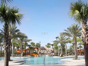 A pool area with palm trees, a water slide, and a rocky backdrop.
