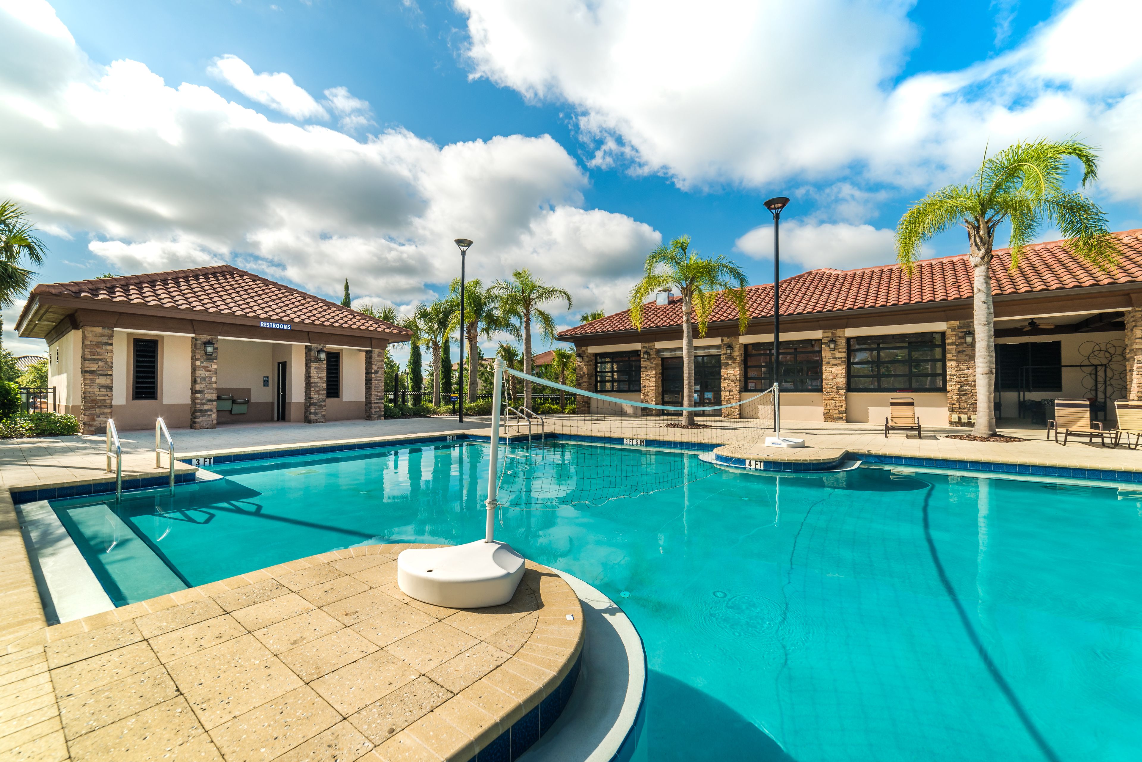 A swimming pool with a tiled deck, a lifeguard stand, and a building with a tiled roof and stone facade.