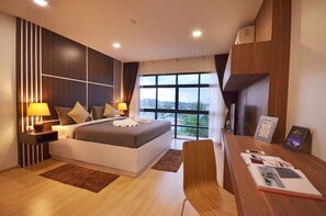 Habitación de hotel moderna con una cama grande, un escritorio con una silla, vista a la ciudad a través de amplias ventanas y una mesita de noche con una lámpara.