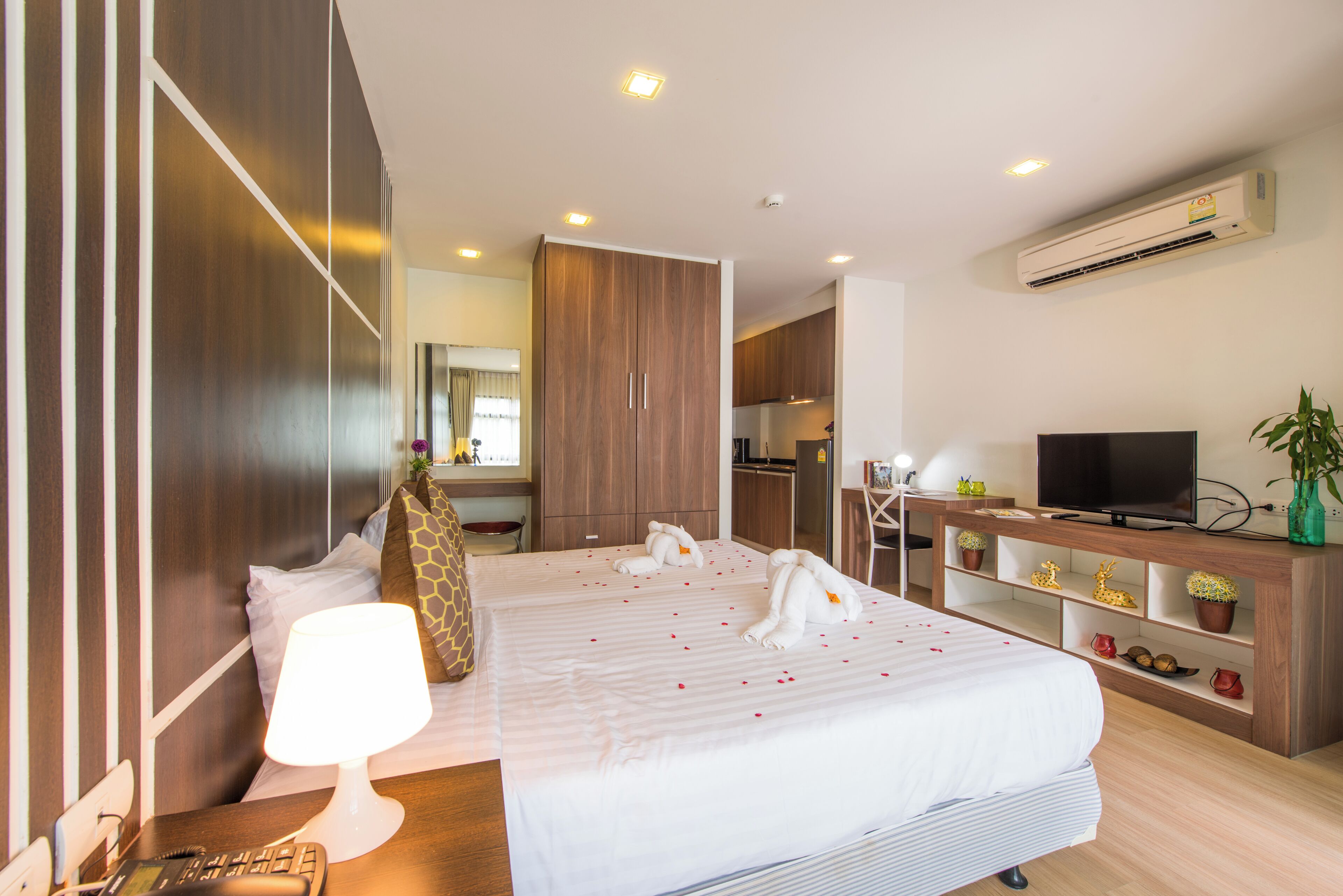 A hotel room with a large bed, a desk with a lamp, a TV, and a minibar.