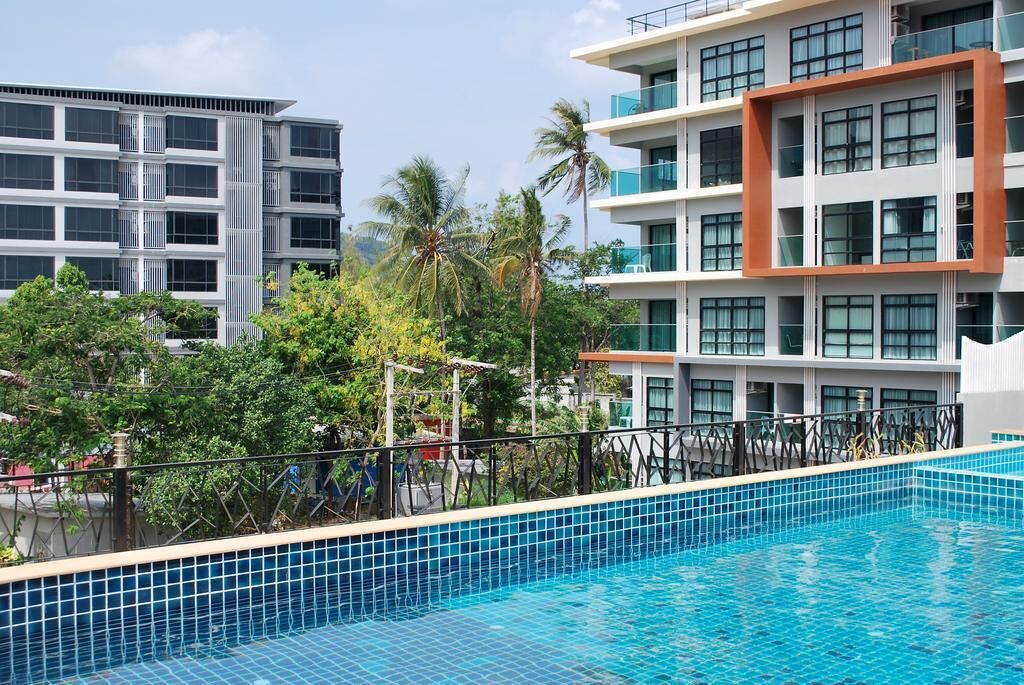 A modern hotel with a swimming pool, surrounded by lush greenery and palm trees.