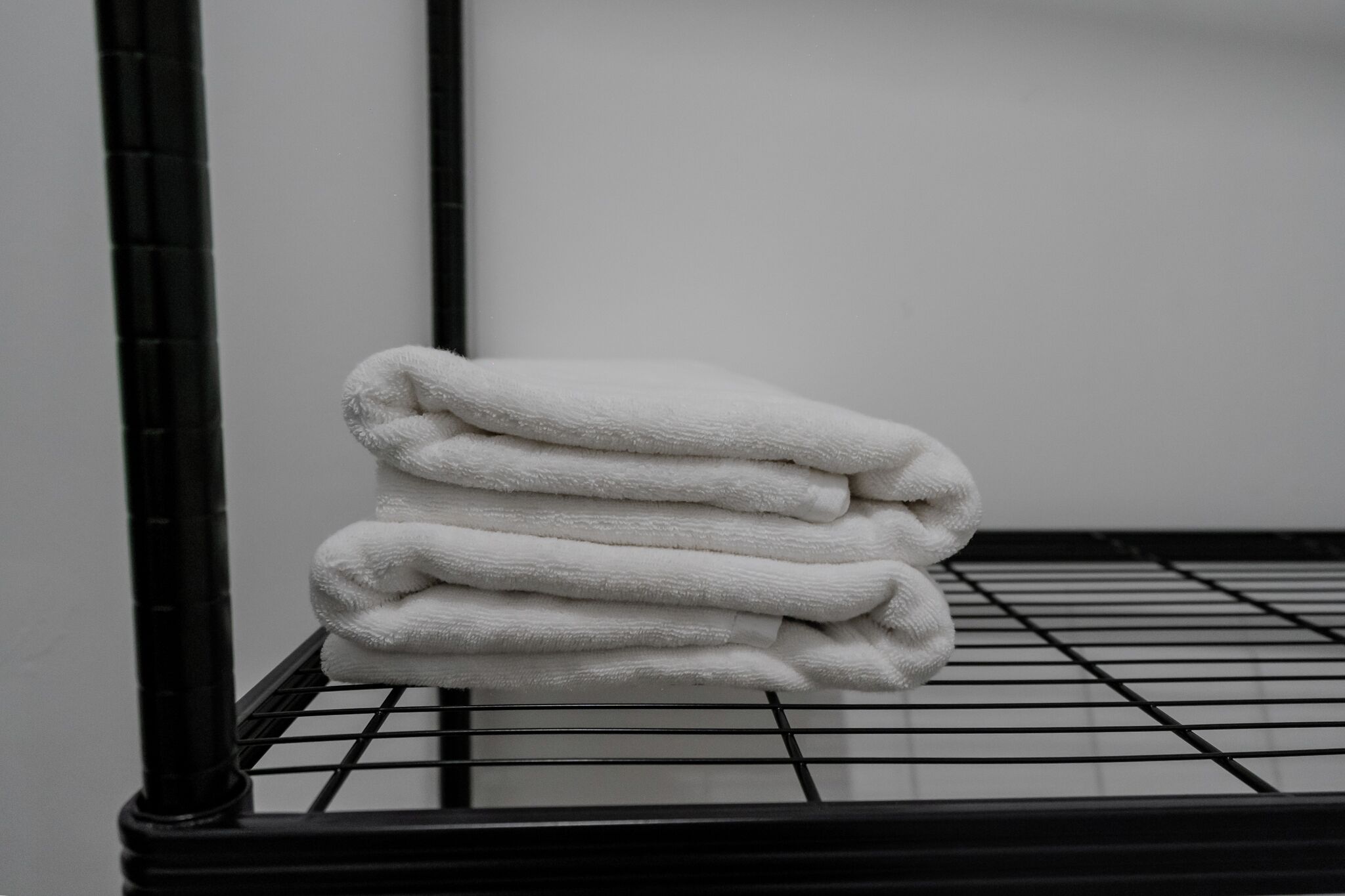 A stack of white towels on a black metal rack in a room with a plain white wall.