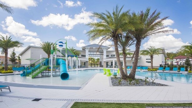 Un espace piscine avec un toboggan, des palmiers et un bâtiment à la façade blanche.