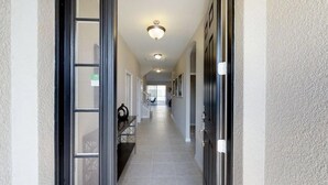 Un couloir avec un sol carrelé, un luminaire au plafond et une porte sur le côté droit.