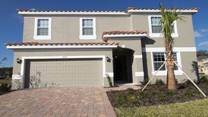 A two-story house with a garage, a small porch, and a palm tree.