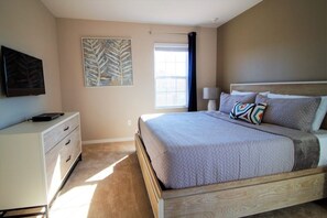 A bedroom with a bed, a nightstand, a TV, and a window with curtains.