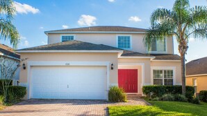 A two-story house with a white garage door, a red door, and a brick driveway. - Ip60154 - Highgate at Legacy Park - 5 Bed 3.5 Baths Villa (Davenport)