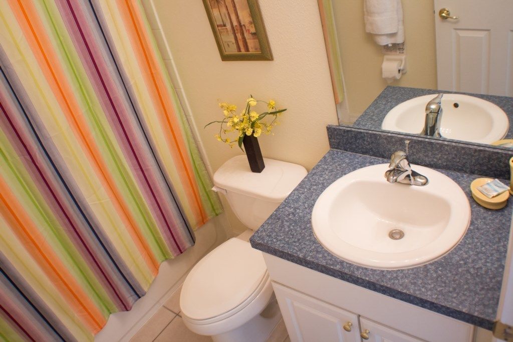 A bathroom with a white toilet, a blue sink with a mirror, and a colorful striped shower curtain.