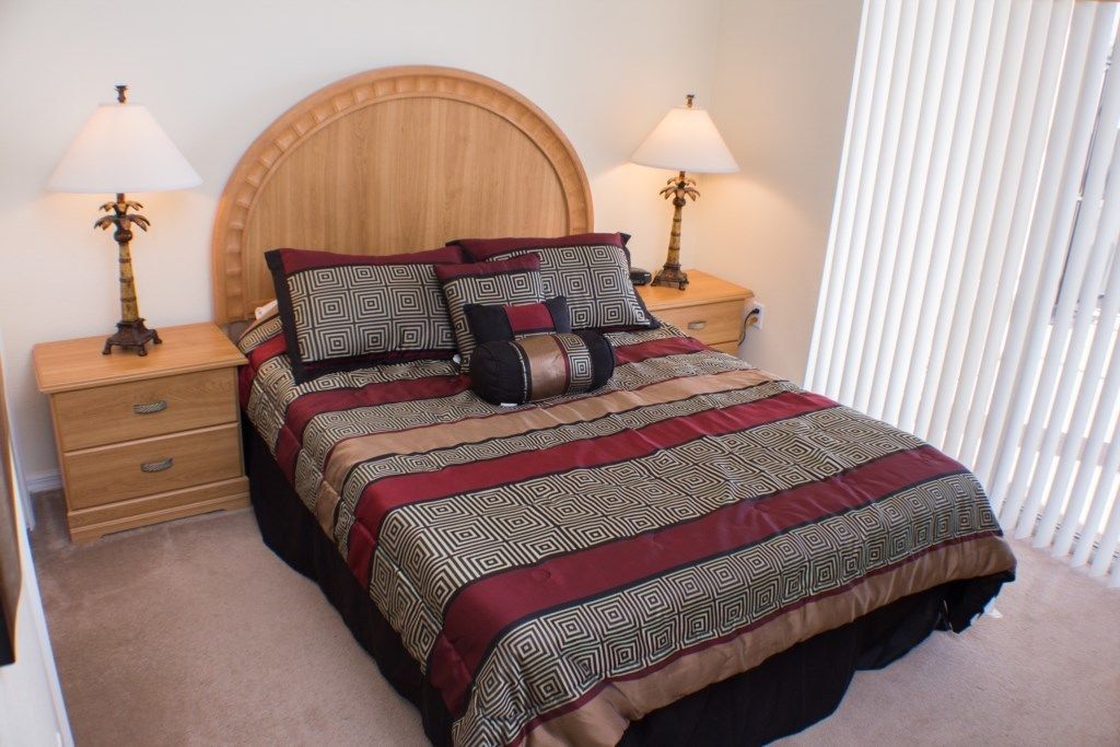 A neatly made bed with patterned bedding, two bedside tables with lamps, and a window with blinds.