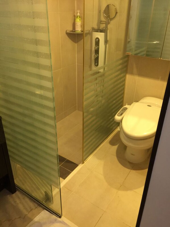 A glass-enclosed shower stall with a toilet and a soap dispenser on a shelf. - Magellan 21 Asterium (Seoul)