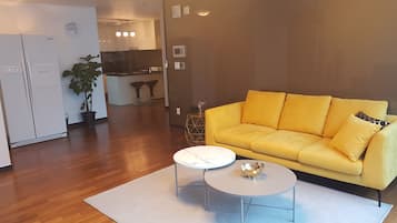 A modern living room with a yellow sofa, a white coffee table, and a kitchen in the background.