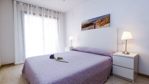 Ein Schlafzimmer mit einem großen Bett, zwei Nachttischen, einer Wandlampe, einem Fenster mit durchsichtigen Vorhängen und einem Bild an der Wand.