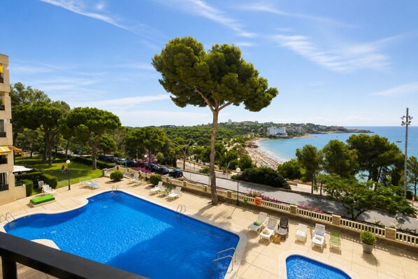 Une piscine avec des chaises longues, un arbre et une vue sur la plage.