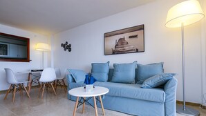 Ein modernes Wohnzimmer mit einem hellblauen Sofa, einem runden weißen Couchtisch und einem Essbereich mit Tisch und Stühlen.