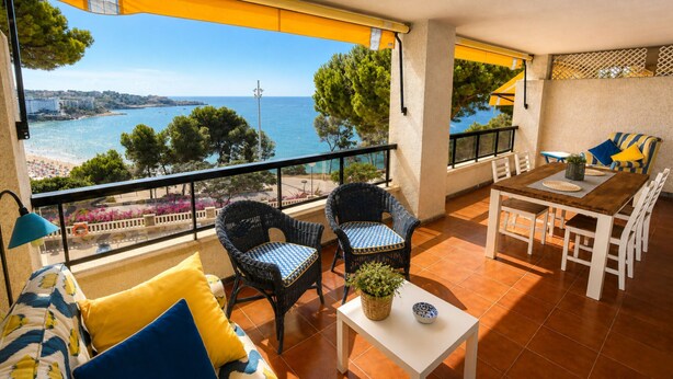 Ein Balkon mit Korbstühlen, einem Tisch und einer Couch mit blau-gelben Kissen.