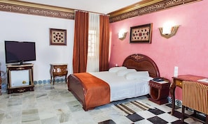 A hotel room with a bed, a television, a bedside table, a nightstand, and decorative wall sconces. - Dar Diaf Cheraga (Algiers)