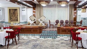 Un comedor formal con una mesa larga, sillas rojas y un escenario con fondo decorativo.