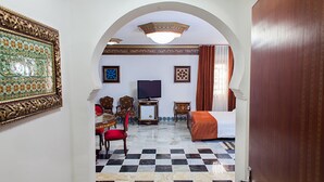 Una habitación de hotel con piso a cuadros, una cama, un televisor, un escritorio con silla y un adorno en la pared.