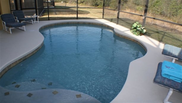 Une piscine à bord incurvé, entourée d’une terrasse avec des chaises longues et un petit jacuzzi.