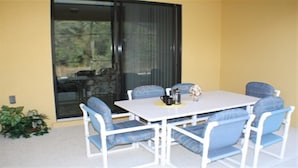 Une terrasse avec une table blanche et des chaises bleues, une cafetière et un objet décoratif posé sur la table.