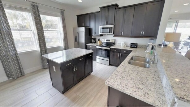 A modern kitchen with dark cabinets, a granite countertop, stainless steel appliances, and a large window. - Aco233851 - The Encore Club Resort - 6 Bed 6.5 Baths Villa (Kissimmee)