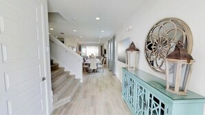 A hallway with a staircase leading to a dining area, a decorative wall with two lanterns, and a light blue console table. - Aco233851 - The Encore Club Resort - 6 Bed 6.5 Baths Villa (Kissimmee)