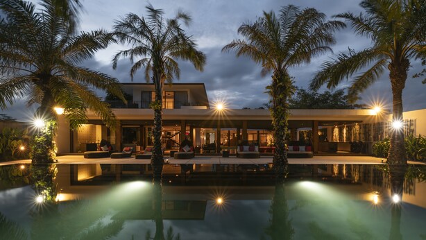 Een modern resort met een zwembad, palmbomen en een verlicht terras.