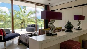 Een moderne kamer met een groot raam, een bed, een bank en een zithoek met een tafel en stoelen.