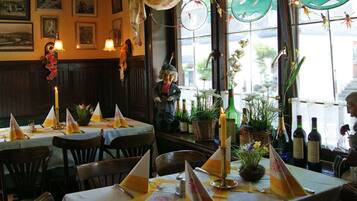 Un restaurante con mesas dispuestas para comer, decorado de forma tradicional con cuadros en las paredes y una variedad de plantas y flores sobre las mesas.