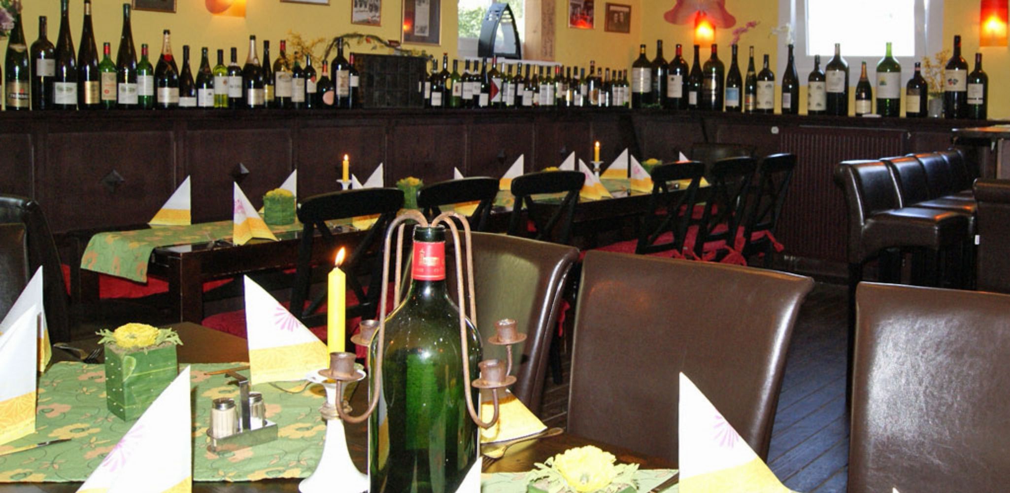 Ein Restaurantinneres mit mehreren Tischen, jeder Tisch ist mit einer Kerze, einer Flasche und einem Servietttuch gedeckt.