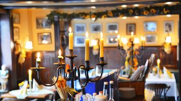 A dining area with multiple candle-lit tables, framed pictures on the wall, and a warm ambiance.