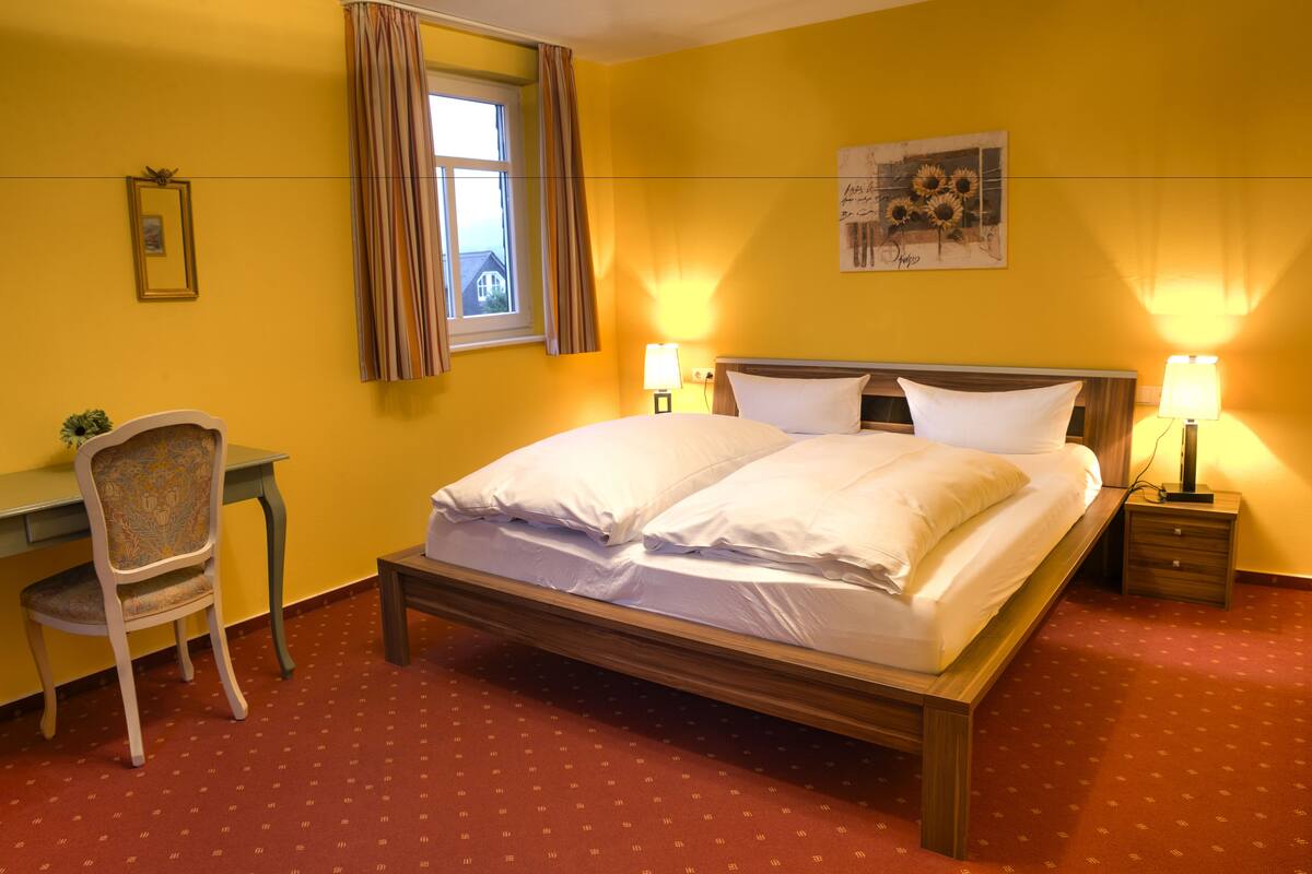 A hotel room with a bed, bedside tables, a desk, and a chair.