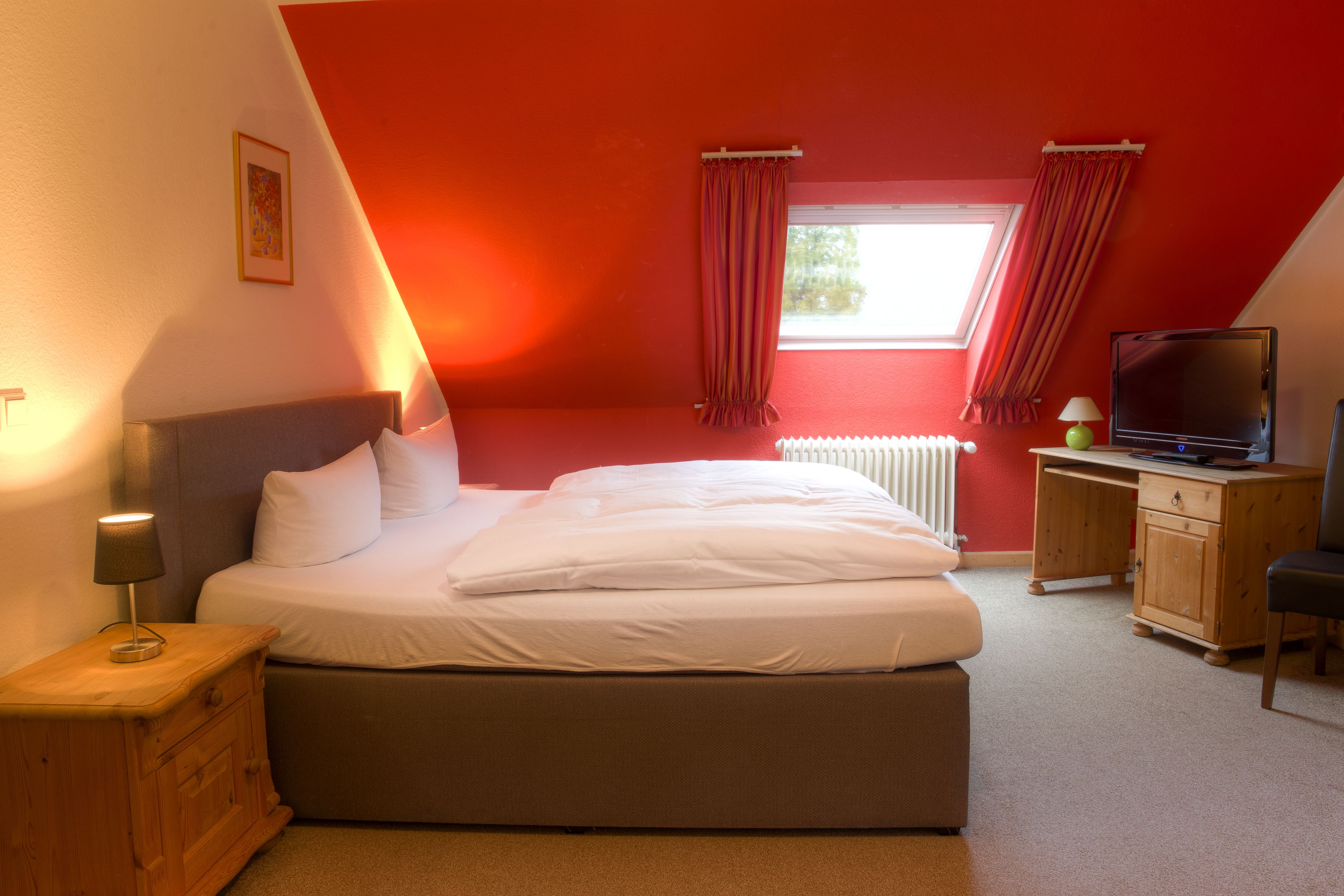 Une chambre à coucher avec un lit, un bureau, une chaise, une télévision et une fenêtre avec des rideaux.