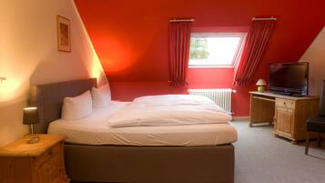 Une chambre à coucher avec un lit, un bureau, une chaise, une télévision et une fenêtre avec des rideaux.