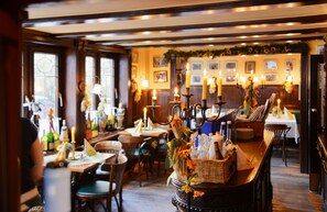 A restaurant interior with wooden tables, chairs, candles, and a bar area with bottles. - Hotel Stoffels (Schmallenberg)