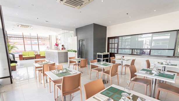Un restaurante moderno con varias mesas y sillas, una zona de bar, y grandes ventanales con vistas a la calle.