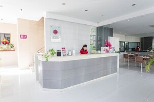Zona de recepción de hotel con diseño moderno, que incluye un mostrador de recepción, un reloj y un área de estar con mesas y sillas.