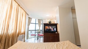 Una habitación de hotel con cama, televisión, ventana con cortinas y balcón con una silla.