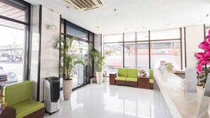 Un vestíbulo de hotel con mostrador de recepción, asientos verdes, ventanas amplias y plantas en macetas.