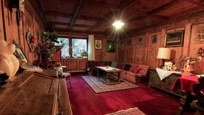 A cozy room with wooden walls, a red carpet, a sofa, a table, and a window with a view of trees. - Hotel Panorama (Cavalese)