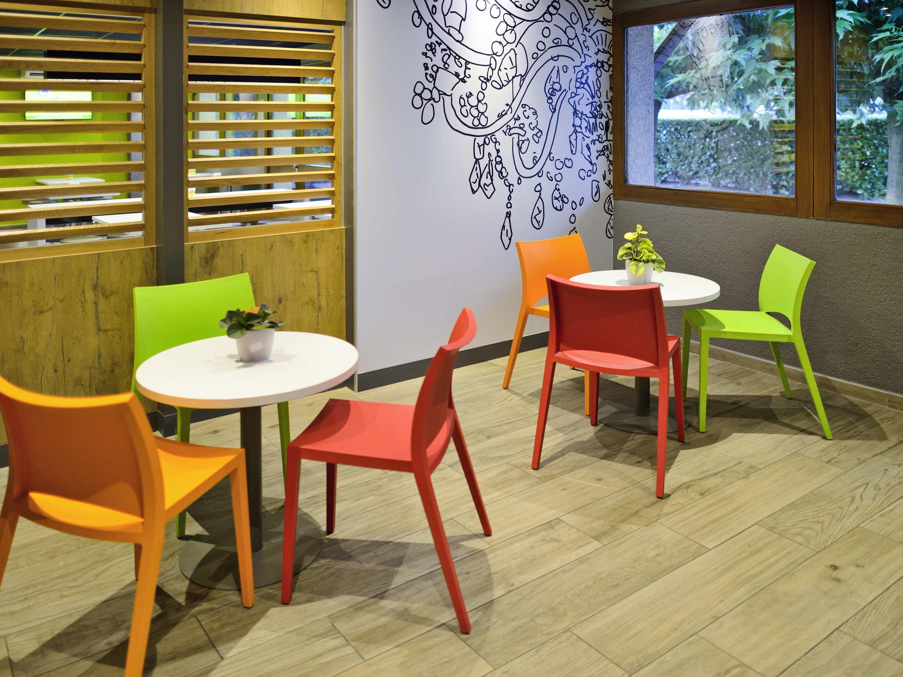 Un intérieur moderne avec des tables rondes et des chaises colorées, un mur à lattes de bois et une fresque murale décorative.