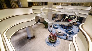 A multi-level hotel lobby with a central seating area, a decorative hanging structure, and a plant arrangement. - Pullman Zhoushan Seaside (Zhoushan)