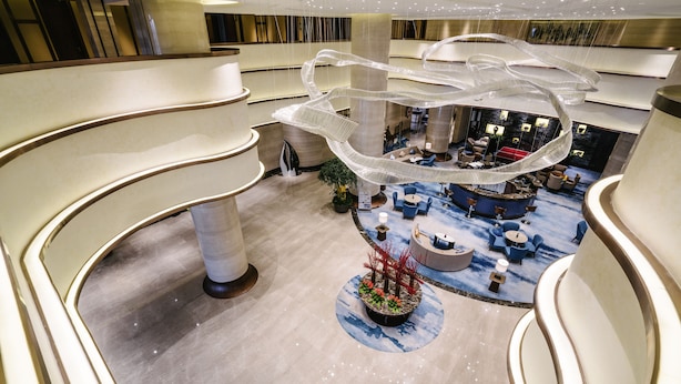 A multi-level hotel lobby with a central seating area, a decorative hanging structure, and a plant arrangement. - Pullman Zhoushan Seaside (Zhoushan)