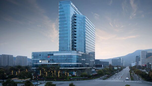 A modern high-rise building with a curved glass facade, located in an urban setting with a clear sky. - Pullman Zhoushan Seaside (Zhoushan)